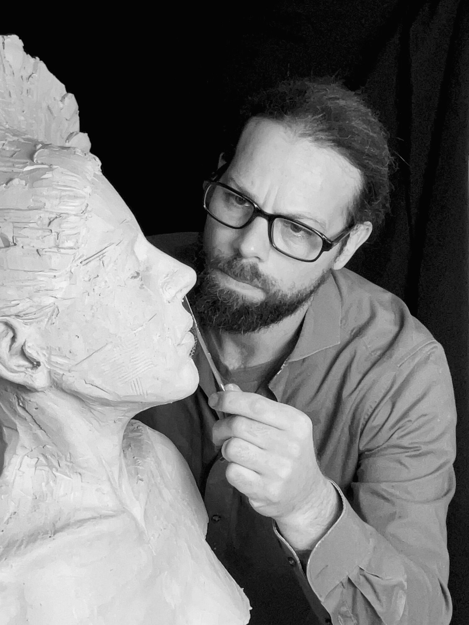 Schwarz-Weiß-Foto des Künstlers Sven Offenbächer mit einer hellen Steinskulptur auf der linken Bildhälfte im Vordergrund.