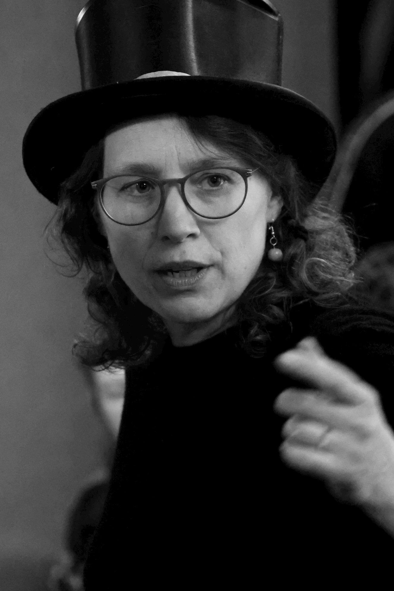 Schwarz-Weiß-Foto der Künstlerin Miriam Lange mit einer Brille, Zylinder und gestikulierend
