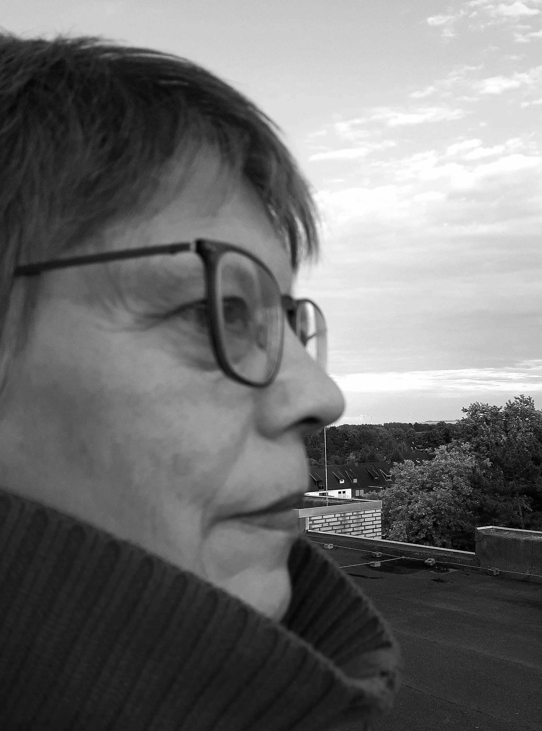 Schwarz-Weiß-Foto der Künstlerin Maria Gust im Profil im Hintergrund Bäume, Himmel, Dach
