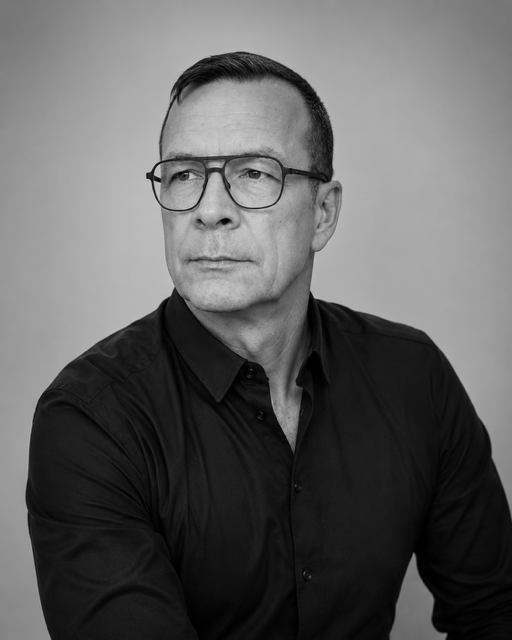 Schwarz-Weiß-Foto des Künstlers Thomas Klitzke-Mandryka mit einem schwarzen Hemd, kurzen Haaren und einer Brille
